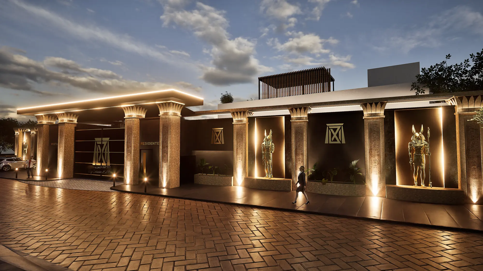 Acceso del residencial al anochecer, con una persona caminando frente a las columnas y las estatuas en nichos